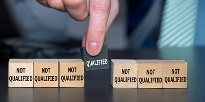 a hand picks up a black block labeled "Qualified" from a row of six other wooden blocks labeled "Not Qualified"