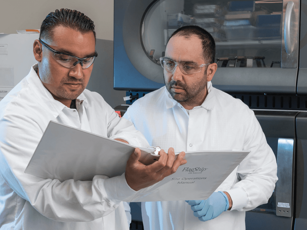 Two lab staff review notes in a binder Two lab staff review notes in a binder